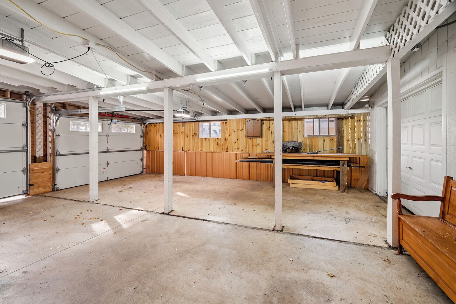 A spacious garage with a concrete floor, wooden walls, and a white ceiling with exposed beams.