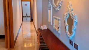 Un pasillo con un banco de madera, un aplique de pared y varios espejos decorativos.