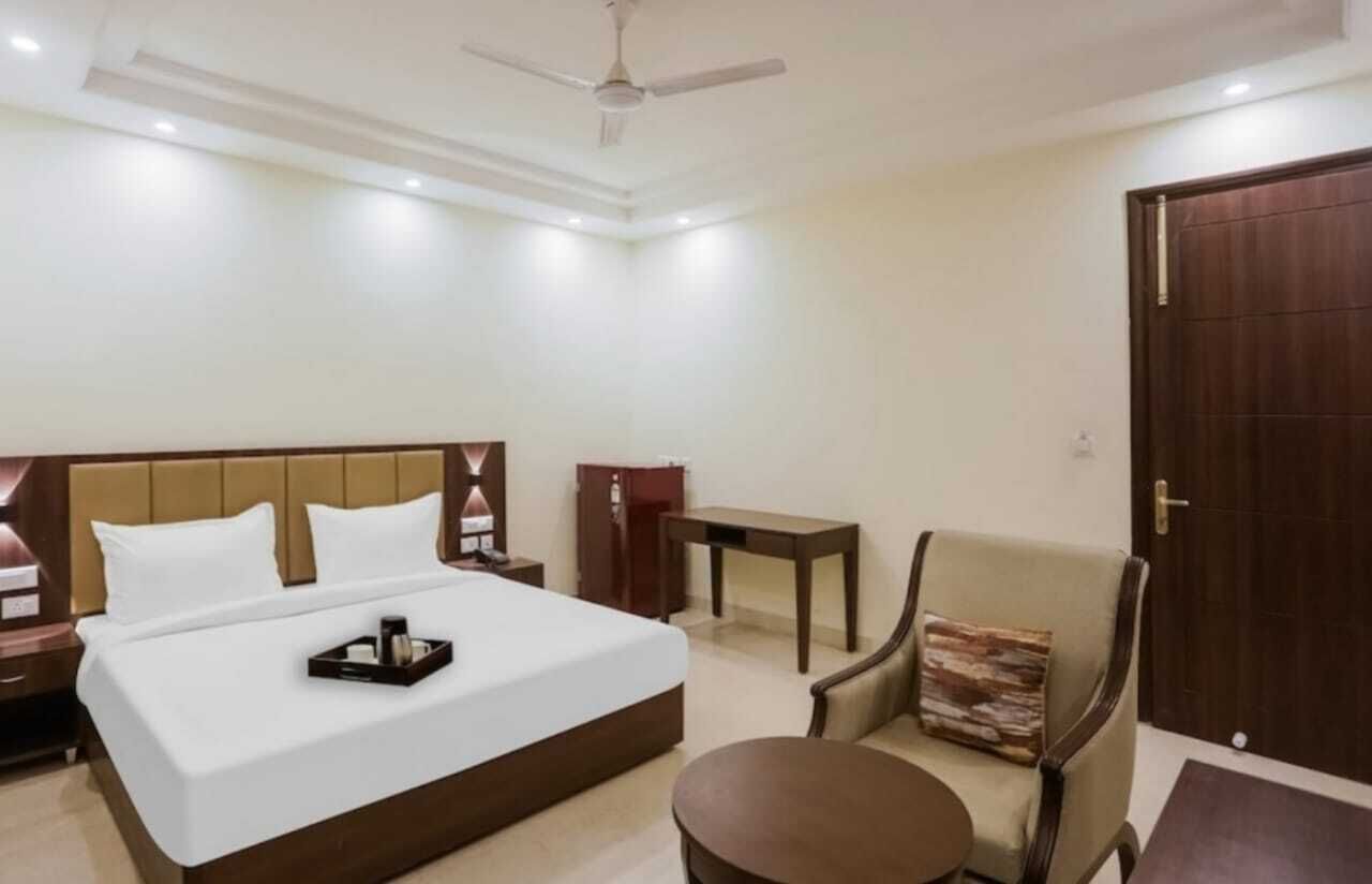 A hotel room with a bed, bedside tables, a chair, a small table, and a door.