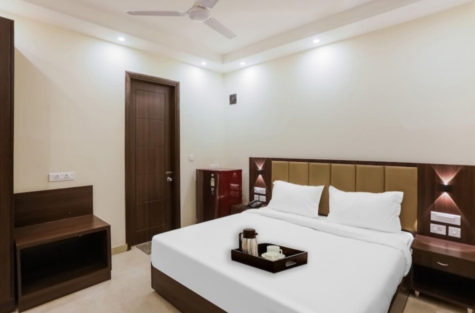 A hotel room with a large bed, a bedside table, a nightstand, a wardrobe, and a ceiling fan.
