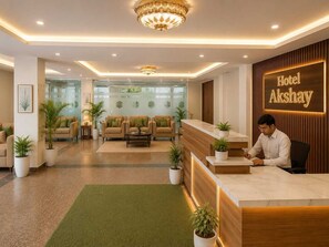 A hotel reception area with a reception desk, sofas, and potted plants. - Akshay Hotel (Gurugram)