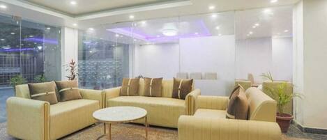 A modern lobby with a large seating area, a round coffee table, and a large window offering a view of the outside.