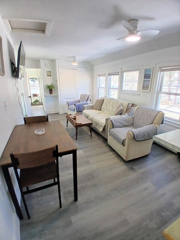 A living room with a wooden dining table, two sofas, a ceiling fan, and large windows.