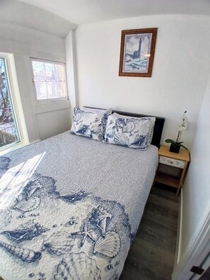 A bedroom with a bed, a nightstand, a window, and a framed picture on the wall.