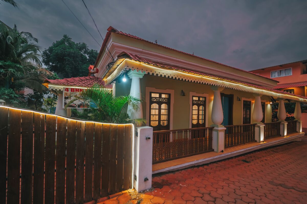 A two-story building with a red-tiled roof, a covered porch with columns, and a sign reading '4 BHK.'