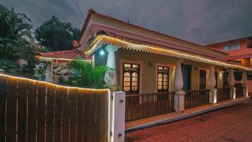A two-story building with a red-tiled roof, a covered porch with columns, and a sign reading '4 BHK.'