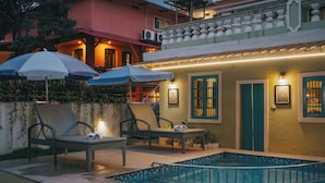 A pool area with lounge chairs and umbrellas, a small pool, and a building with a balcony. - Baga Villa Harshita (Calangute)