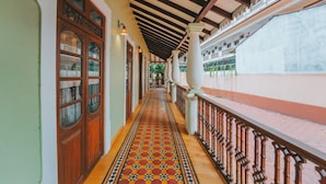 A corridor with patterned flooring, wooden doors, and a balcony with a railing. - Baga Villa Harshita (Calangute)