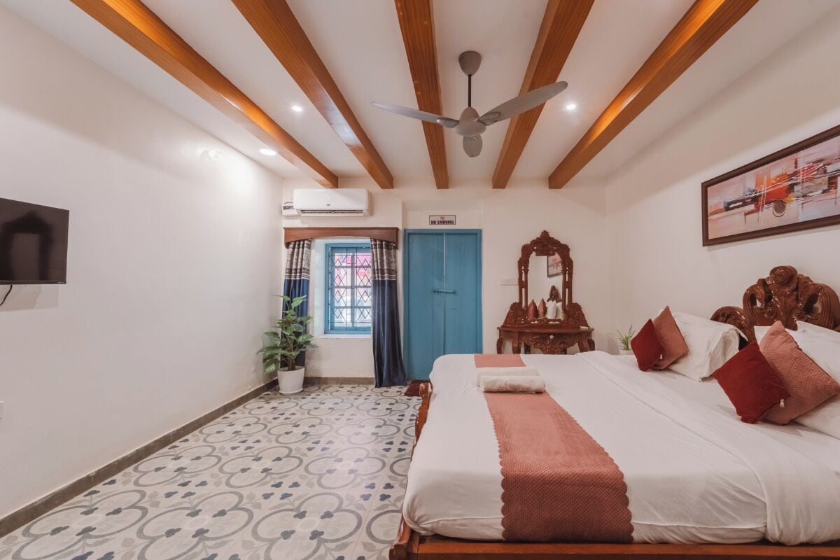 Une chambre à coucher avec un lit, un ventilateur de plafond, une télévision, une porte et une fenêtre avec des rideaux.