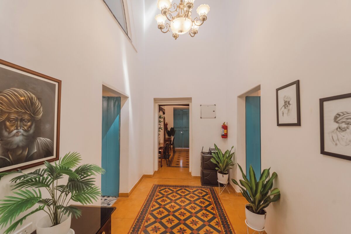 A hallway with a patterned rug, potted plants, framed artwork, and a chandelier.