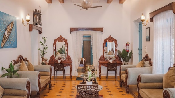 A spacious living room with ornate wooden furniture, a ceiling fan, and a large painting on the wall. - Baga Villa Harshita (Calangute)