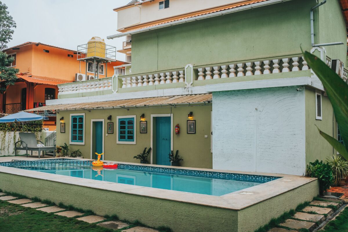 Una piscina con un juguete inflable amarillo, un edificio verde con un balcón blanco y una puerta azul.