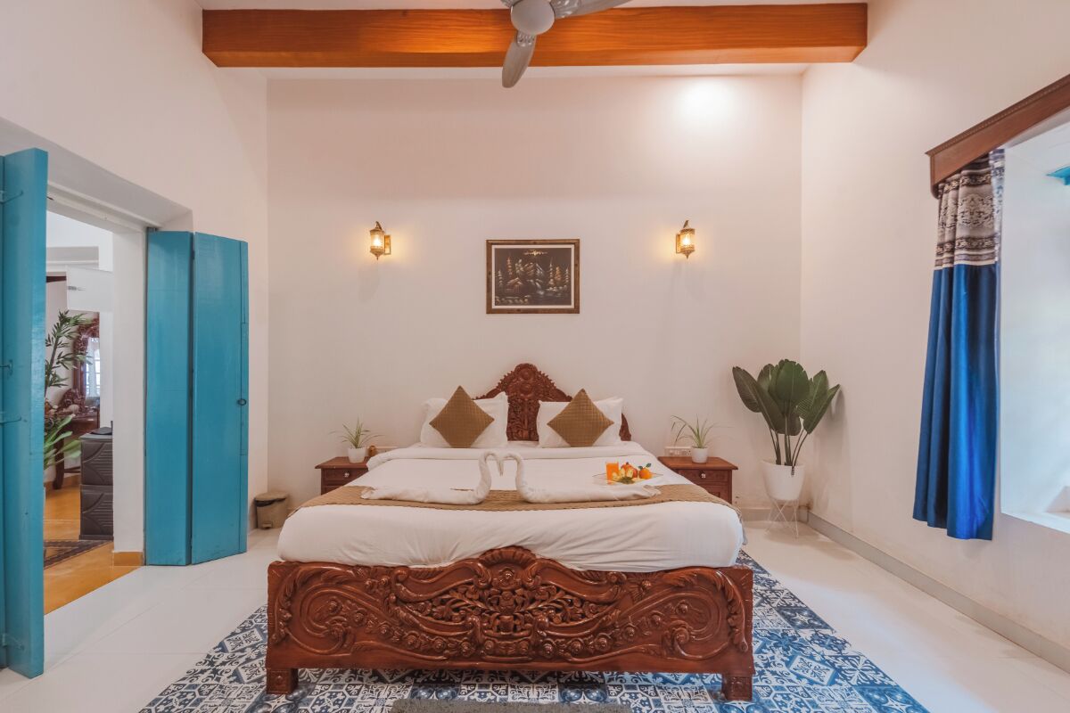 A bedroom with a large bed, two wall sconces, a framed picture, and a potted plant.