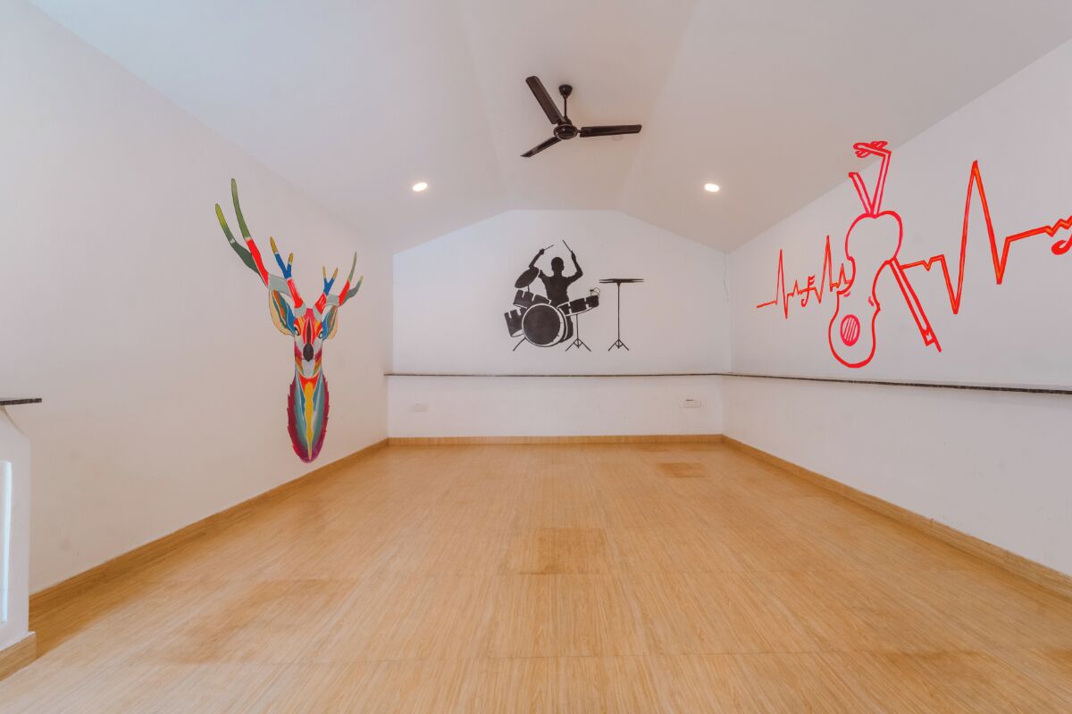 A spacious room with a wooden floor, a ceiling fan, and three wall-mounted artworks depicting a colorful bird, a drummer, and a red line drawing.