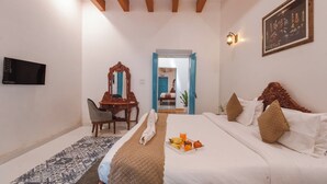 A hotel room with a bed, a desk, a chair, a television, and a painting on the wall. - Baga Villa Harshita (Calangute)