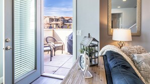 Ein Zimmer mit einer Schiebeglastür, die auf eine Terrasse führt, einem schwarzen Sofa, einer Lampe, einer kleinen Uhr und einer dekorativen Laterne.