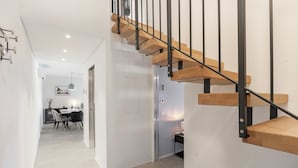 Een modern interieur met een houten trap, een eethoek met tafel en stoelen, en een gang die naar een andere kamer leidt.