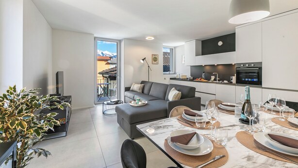 Een moderne woonkamer met een bank, een eettafel voor zes personen en een keuken met apparatuur.