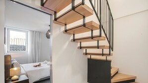 Een moderne hotelkamer met een houten trap, een bed met witte lakens, een bedlampje en uitzicht buiten door een raam.
