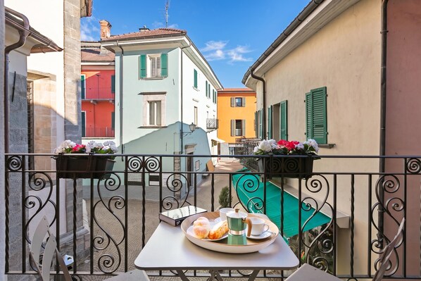 A balcony with a table set for breakfast, overlooking a narrow street with colorful buildings.