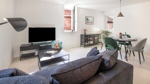 Ett modernt vardagsrum med en platt-TV, ett soffbord med böcker, en soffa och en matplats med ett bord dukat för två personer.