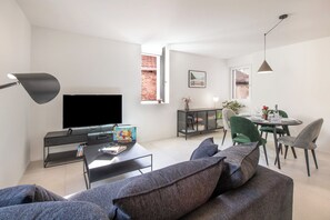 A modern living room with a flat-screen TV, a coffee table with books, a sofa, and a dining area with a table set for two. - Corte di Ascona 1 with AC & Wi‑Fi for 4, Ascona, Switzerland (Ascona)