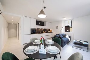 A modern kitchen with white cabinets, a dining area with a round table set for four, and a living area with a grey sofa and a coffee table. - Corte di Ascona 1 with AC & Wi‑Fi for 4, Ascona, Switzerland (Ascona)