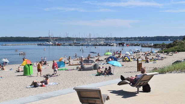 Une plage où l’on voit des gens se prélasser au soleil, des tentes et des bateaux en arrière-plan.
