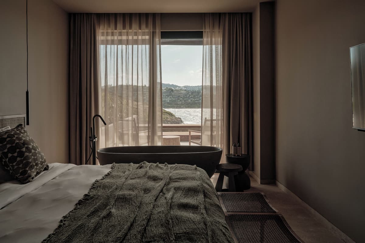 A bedroom with a large bed, a bathtub, and a view of the sea.