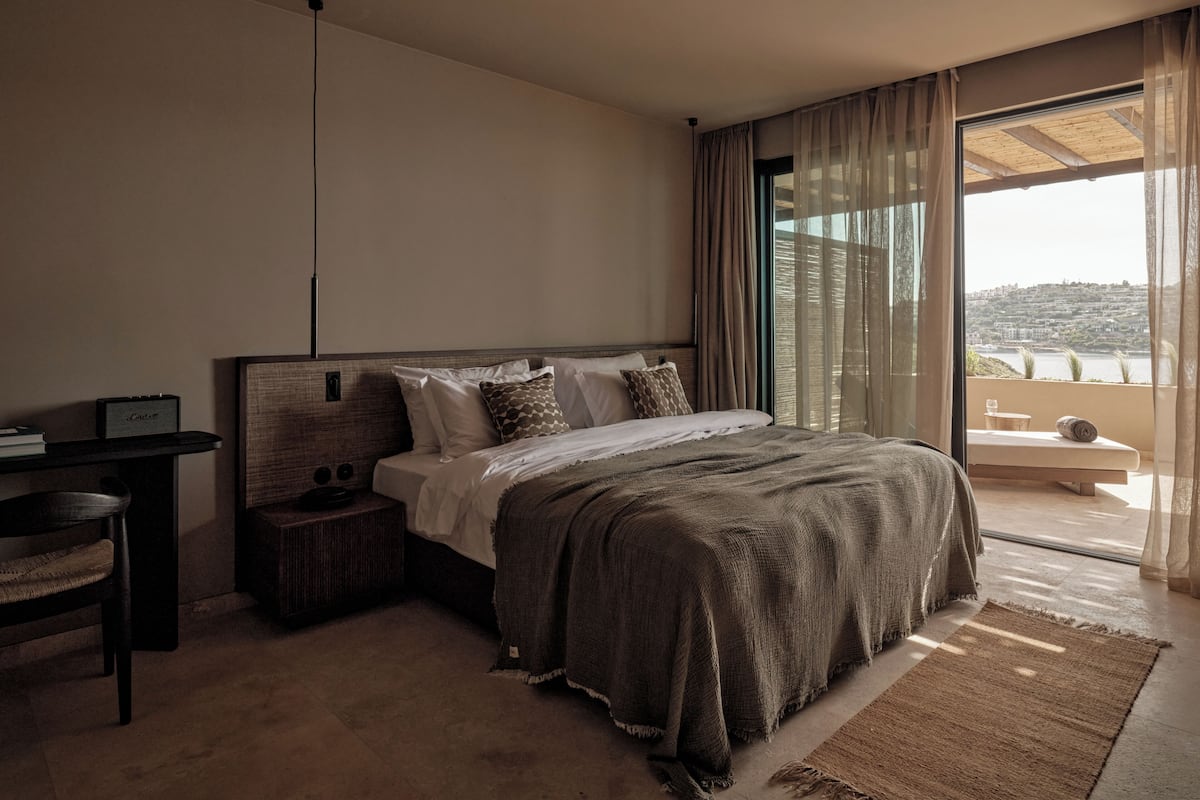 A bedroom with a bed, bedside table, and a view of a hillside.