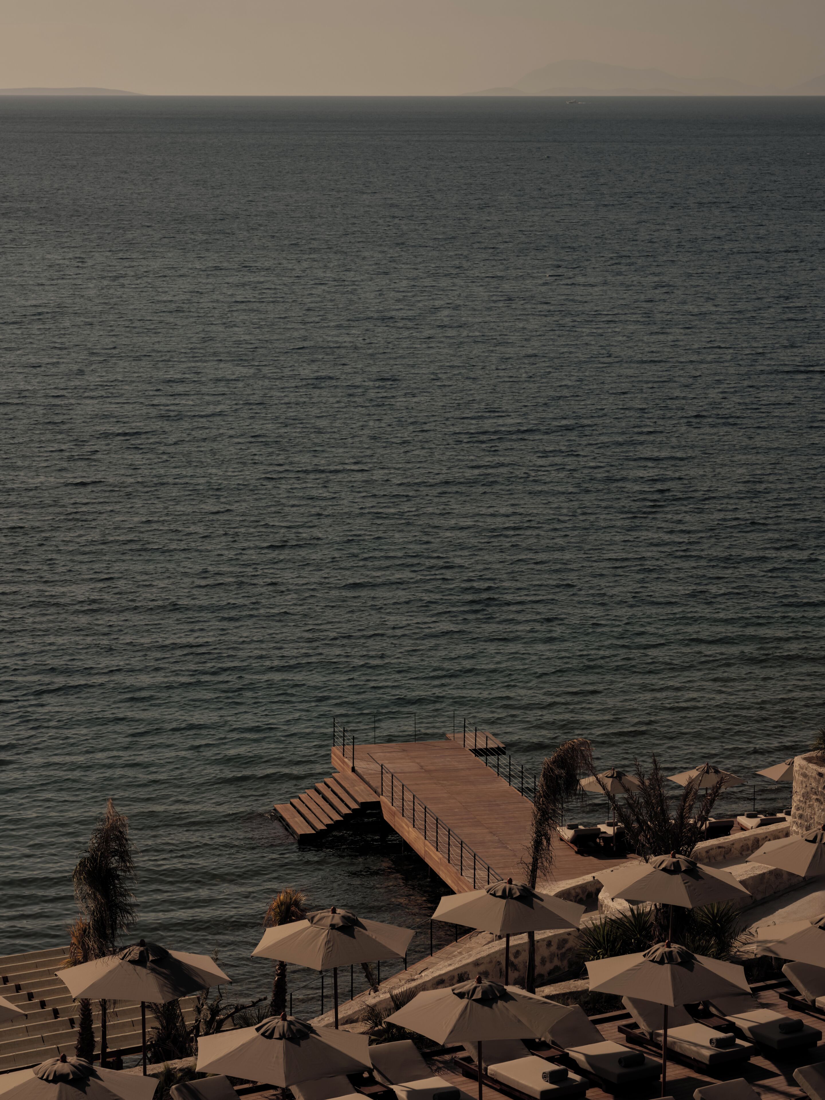Una località balneare con un molo di legno che si protende sul mare, sedie a sdraio e ombrelloni.