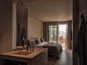 A modern hotel room with a large bed, a bathroom with a large mirror and sink, and a balcony with a view of the sea. - Oku Bodrum (Bodrum)