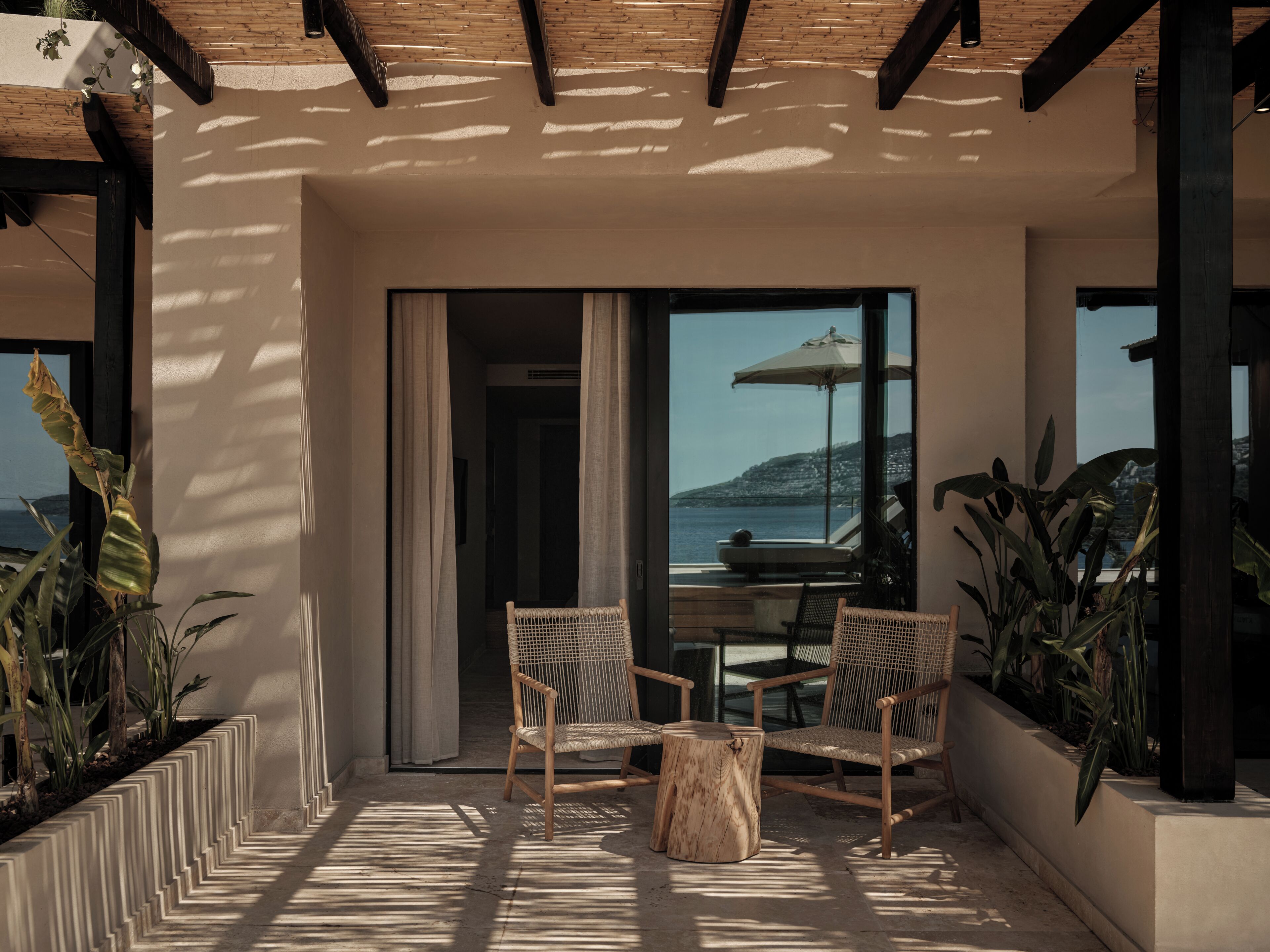 A balcony with wicker chairs, a wooden table, and a view of the sea.