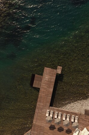 An aerial view of a wooden deck with lounge chairs and umbrellas, overlooking clear water. - Oku Bodrum (Bodrum)