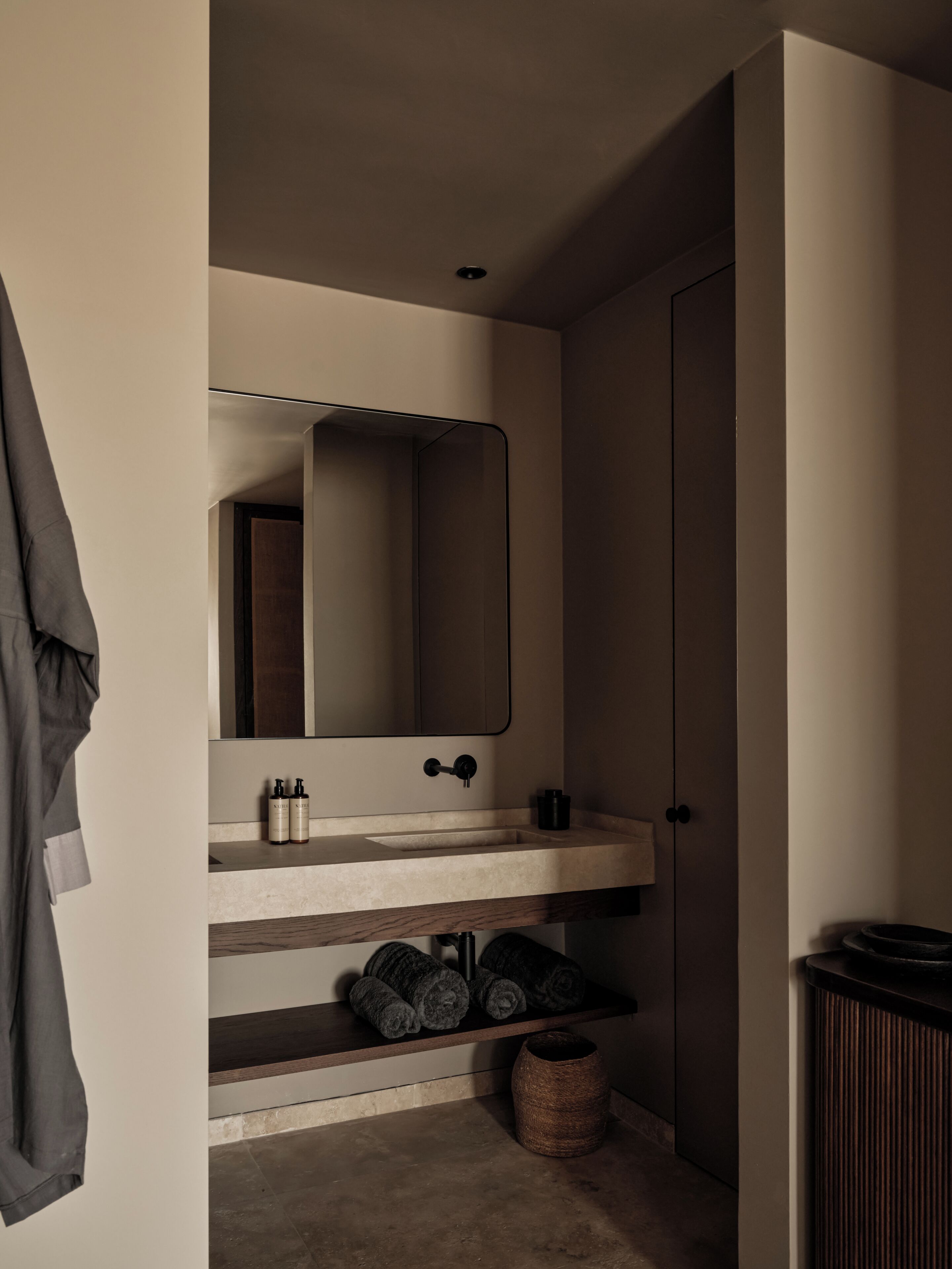 A bathroom with a mirror, sink, towel rack, and a small trash bin.