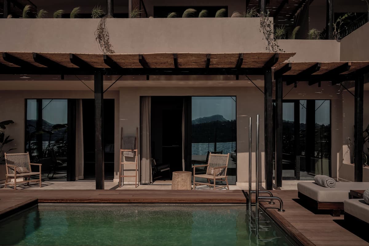 A modern outdoor pool area with a wooden deck, lounge chairs, and a view of the mountains.