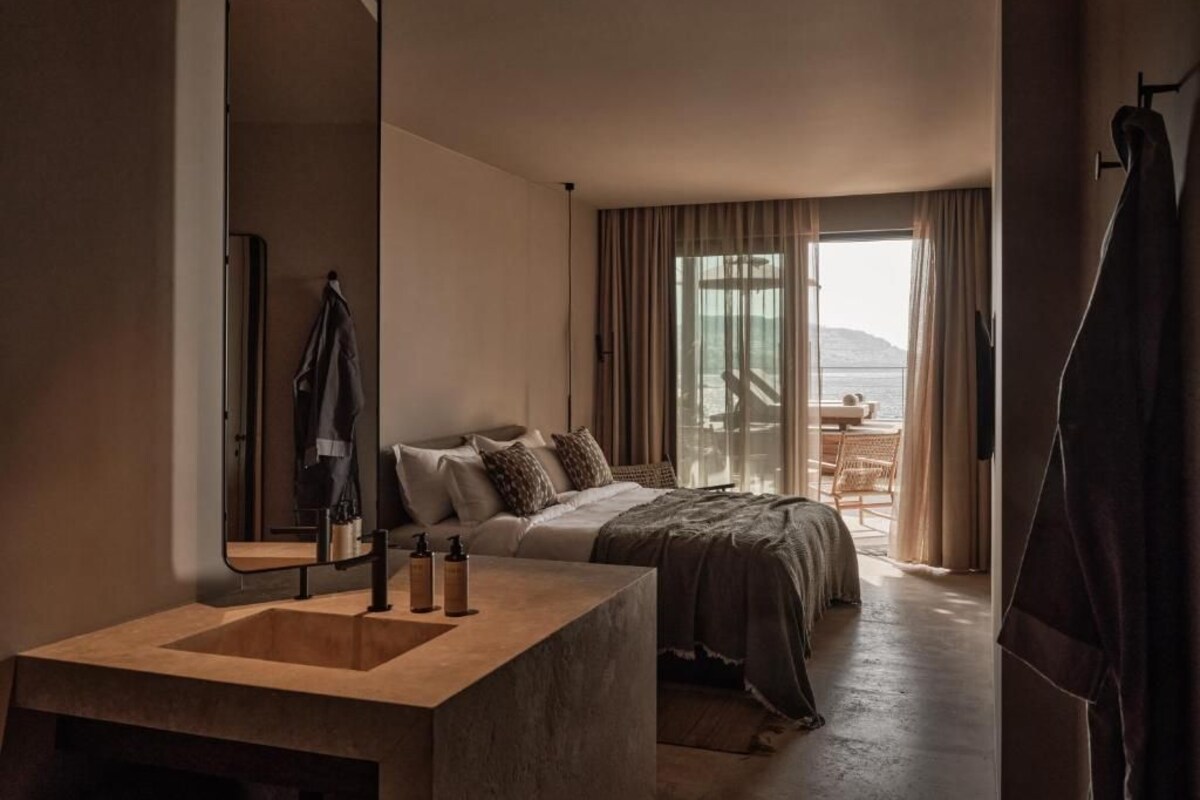 A modern hotel room with a large bed, a built-in sink, and a view of the outdoors.