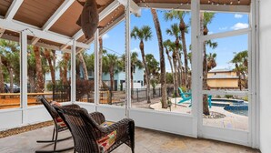 A covered patio with wicker rocking chairs, a pool, and palm trees. - Steps to Beach | Pool + Hot Tub | 2025 Remodeled! (Englewood)