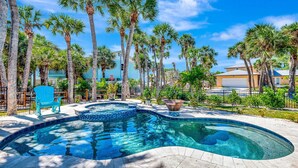 A swimming pool with a curved edge, surrounded by palm trees and a blue chair. - Steps to Beach | Pool + Hot Tub | 2025 Remodeled! (Englewood)