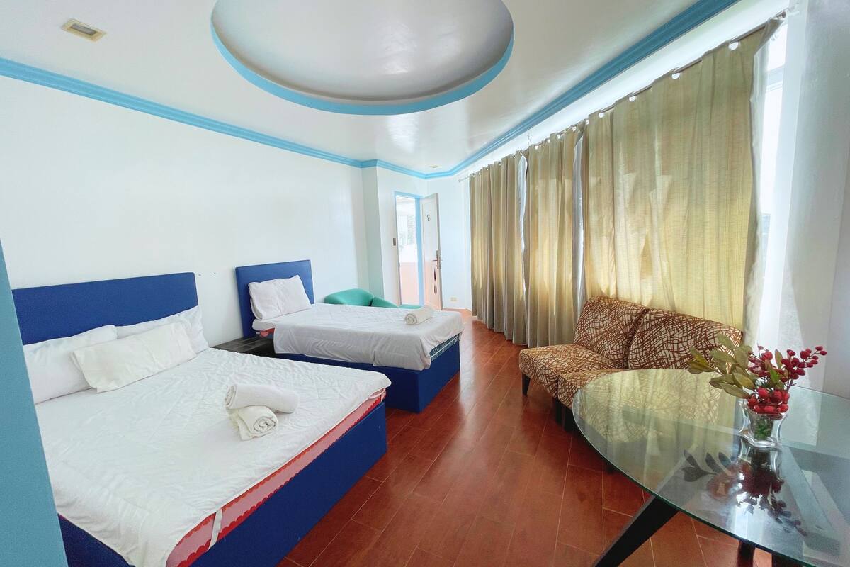 A hotel room with two beds, a sofa, a glass table, and a view of the outside.