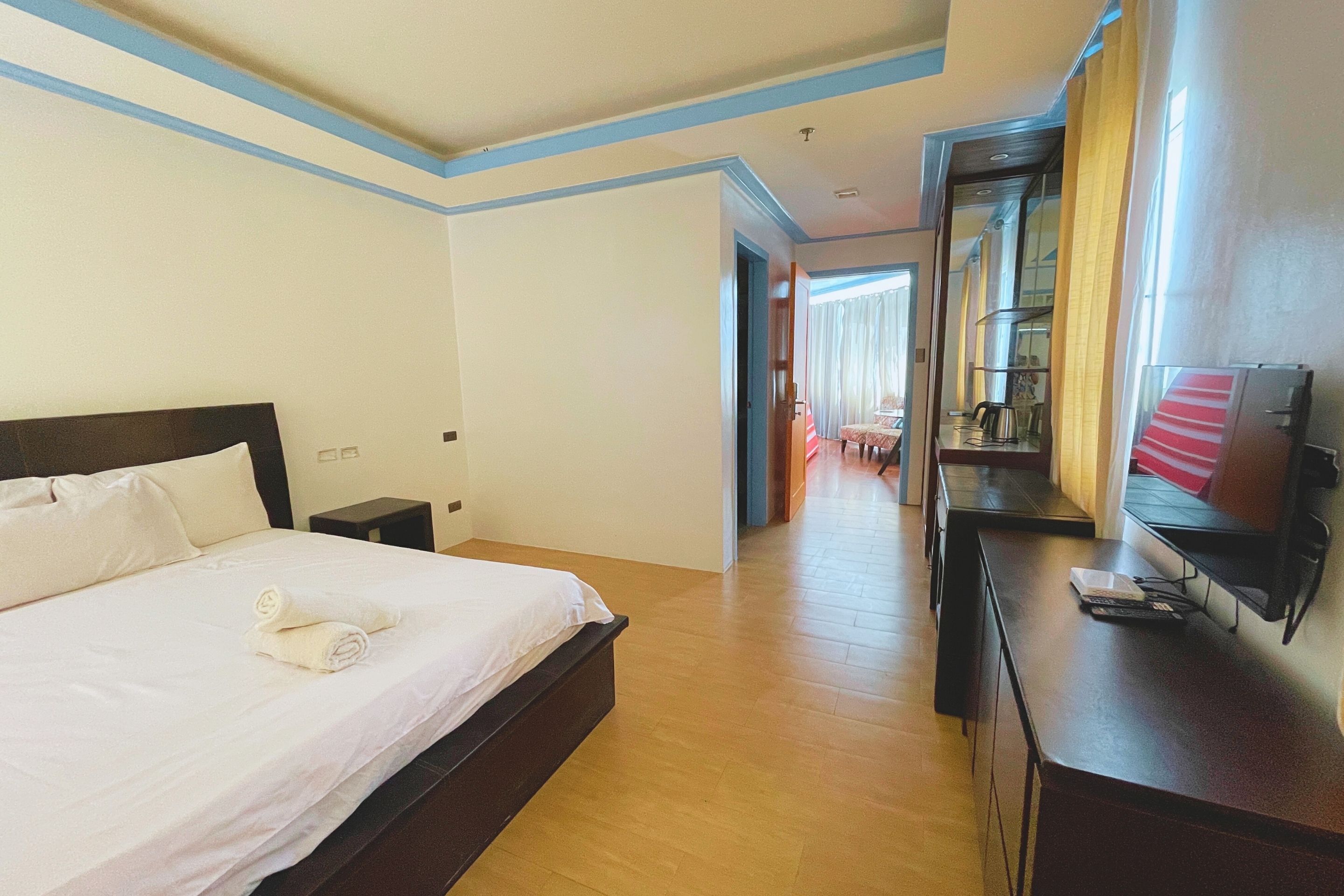 A hotel room with a large bed, a desk, a TV, and a mirror.
