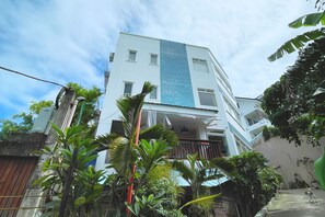 A multi-story building with a white facade and blue stripe, surrounded by lush greenery. - Here Innstead Boracay powered by Cocotel (Boracay Island)