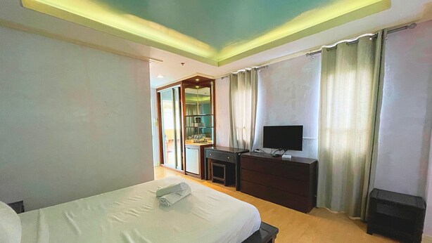 Habitación de hotel con cama, escritorio con televisor, mueble pequeño y ventana con cortinas.