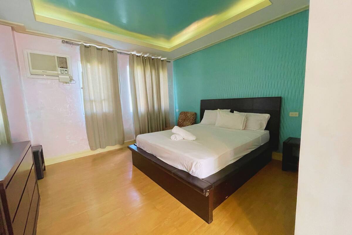 A hotel room with a bed, curtains, a bedside table, and a wall-mounted air conditioner.