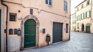 A narrow street with a building featuring a green door and a black garage door. - Casa Milla In Center Town (Lucca)