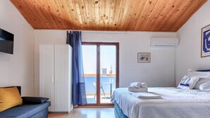 A bedroom with a wooden ceiling, a bed with white bedding, a blue sofa, and a view of the outside through a glass door.