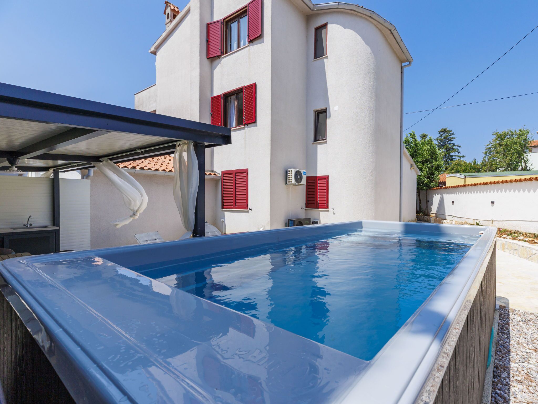 A swimming pool with a covered area, a sink, and a window with red shutters.