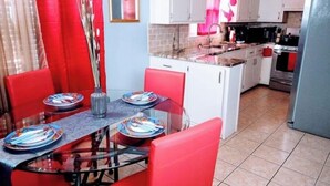 A compact kitchen with white cabinets, a stainless steel refrigerator, and a dining area with red chairs and a glass table. - "Charming Oasis: Sleeps 11: Pool Table: Big screens: Full Kitchen" (Kansas City)
