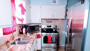 A compact kitchen with white cabinets, a stainless steel stove, a refrigerator, and a sink. - "Charming Oasis: Sleeps 11: Pool Table: Big screens: Full Kitchen" (Kansas City)