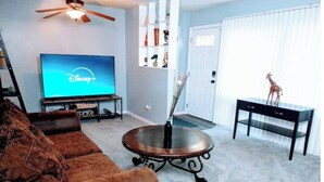 A living room with a brown leather sofa, a round coffee table, a flat-screen TV, and a ceiling fan. - "Charming Oasis: Sleeps 11: Pool Table: Big screens: Full Kitchen" (Kansas City)